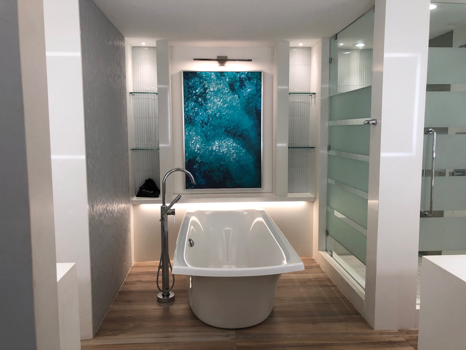 A resort suite bathroom with a freestanding soaking tub beneath a turquoise artwork