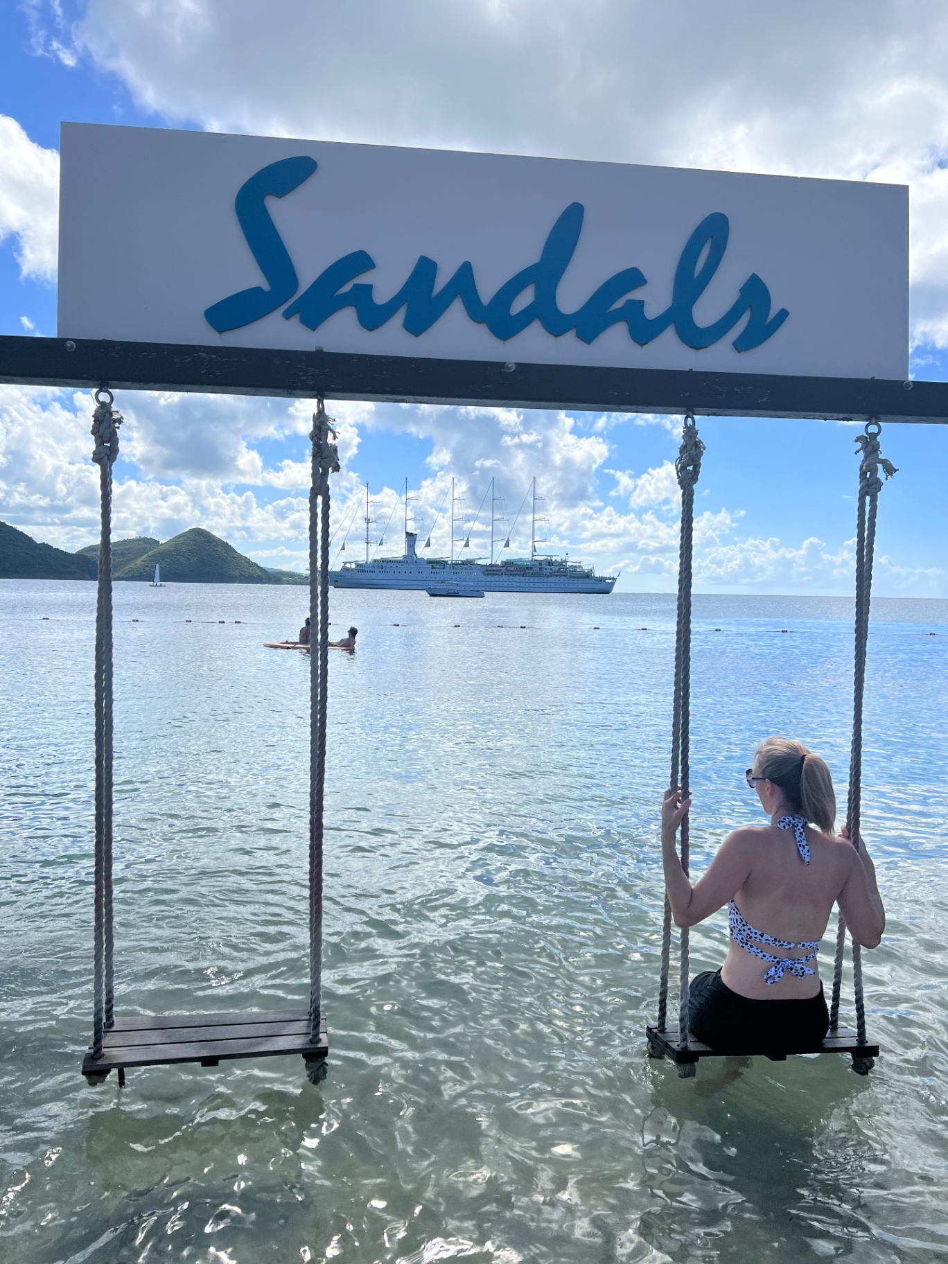 Jen on a wooden swing in shallow turquoise water beside a Sandals sign