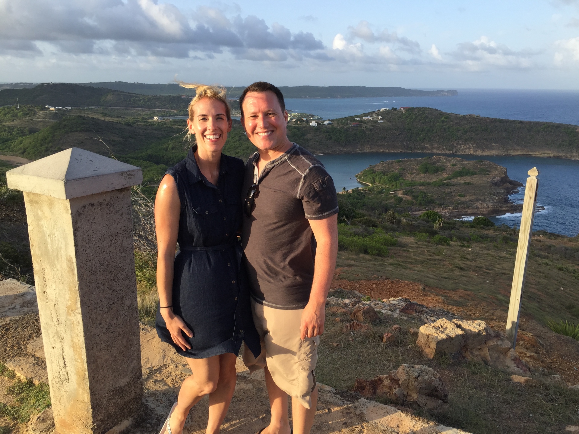 Adam and Jen Conway smiling at a rocky island lookout above a green coastline and bay