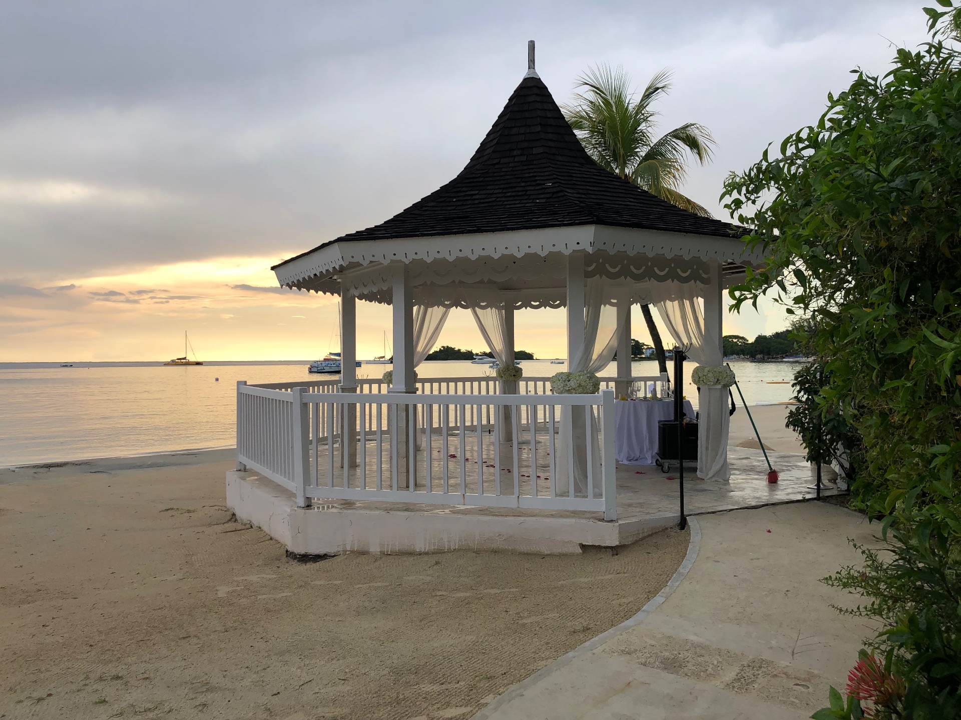 A white beachfront wedding gazebo with draped curtains at dusk