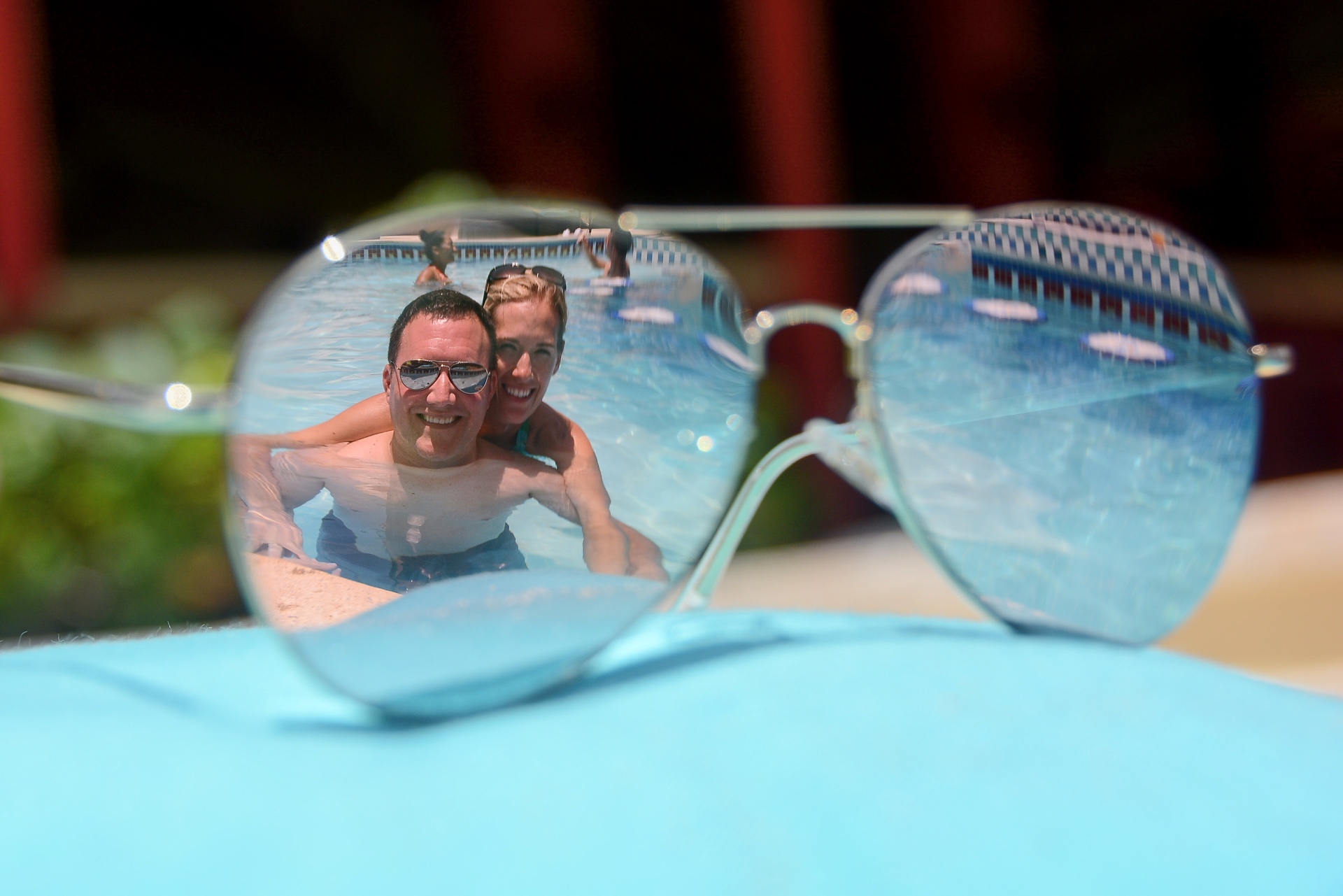 Adam and Jen Conway reflected in a pair of sunglasses resting by a resort pool