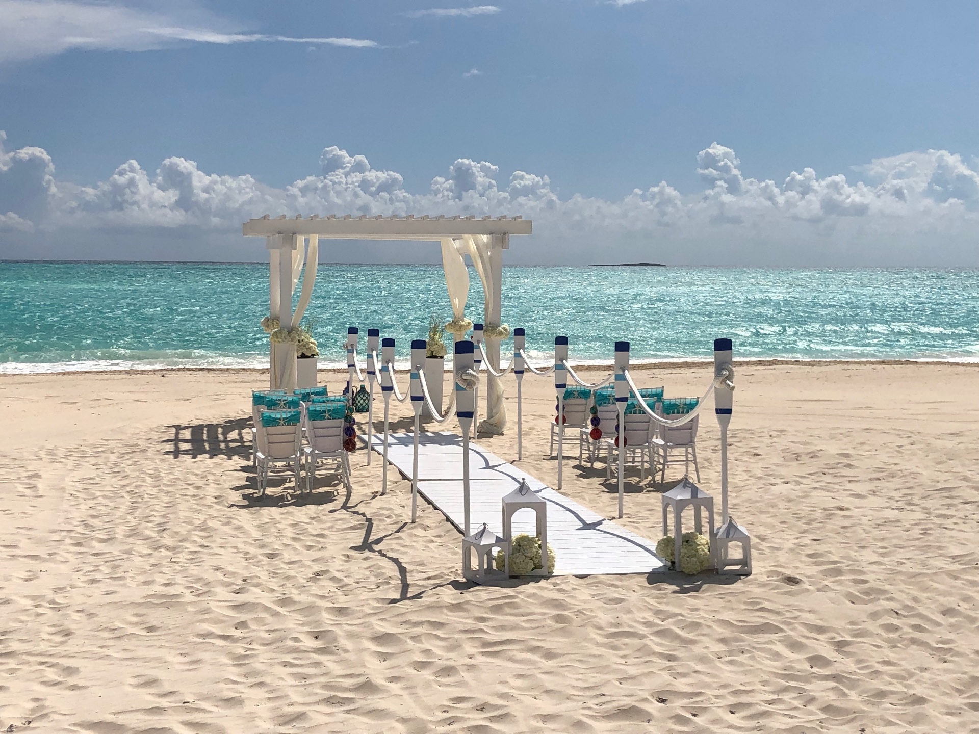 A white beach wedding arbor and aisle set up on turquoise Caribbean water