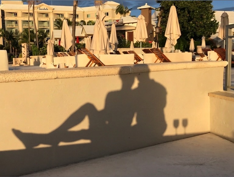 The shadow of Adam and Jen with two wine glasses cast on a wall beside a Sandals resort pool at golden hour